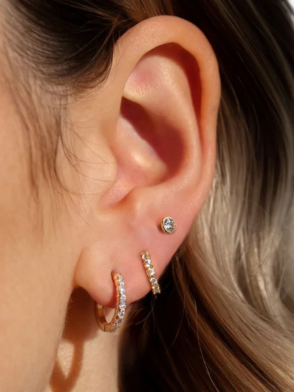 Ear wearing a 14K yellow gold Pavé-All-Day hoop in the lobe, with a gold stud and a second pavé hoop above
